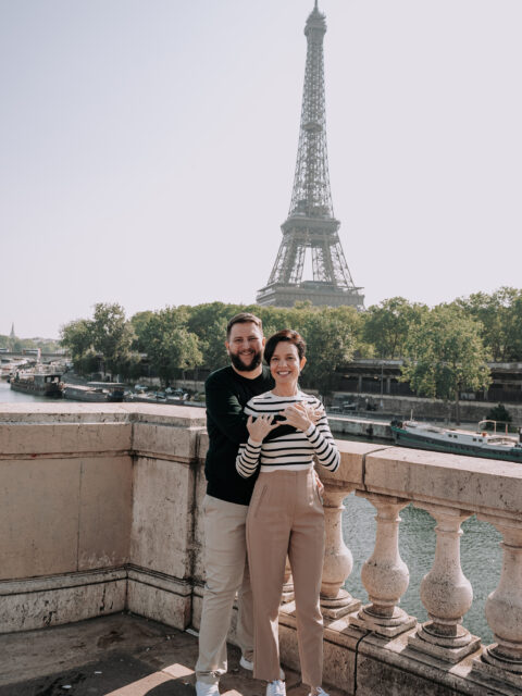Casal com o bebê no colo posando em frente a bicicletas com a Torre Eiffel ao fundo, em ensaio fotografico profissional em Paris