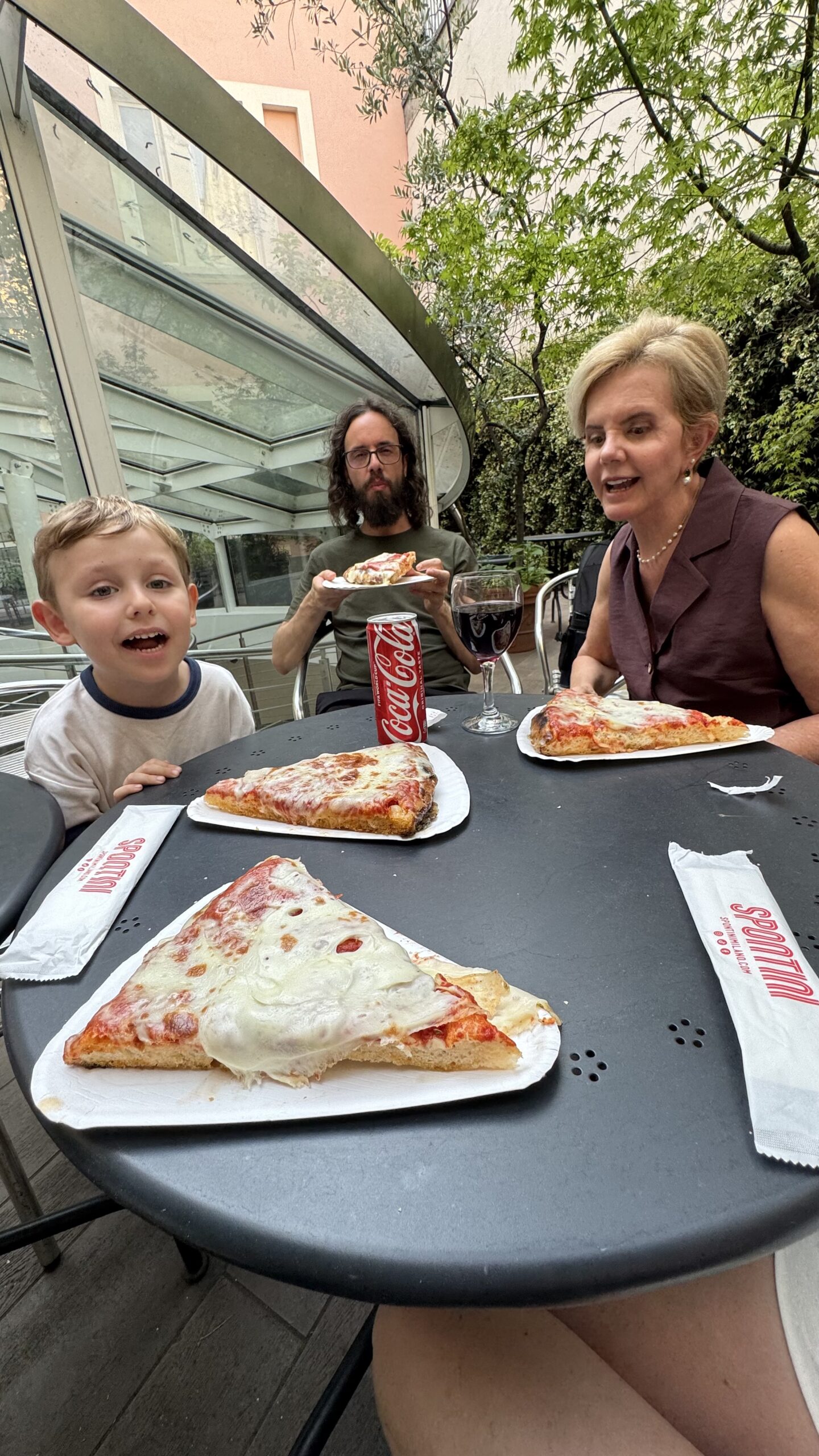 Família sentada à mesa com fatias de pizza al taglio e uma lata de refrigerante