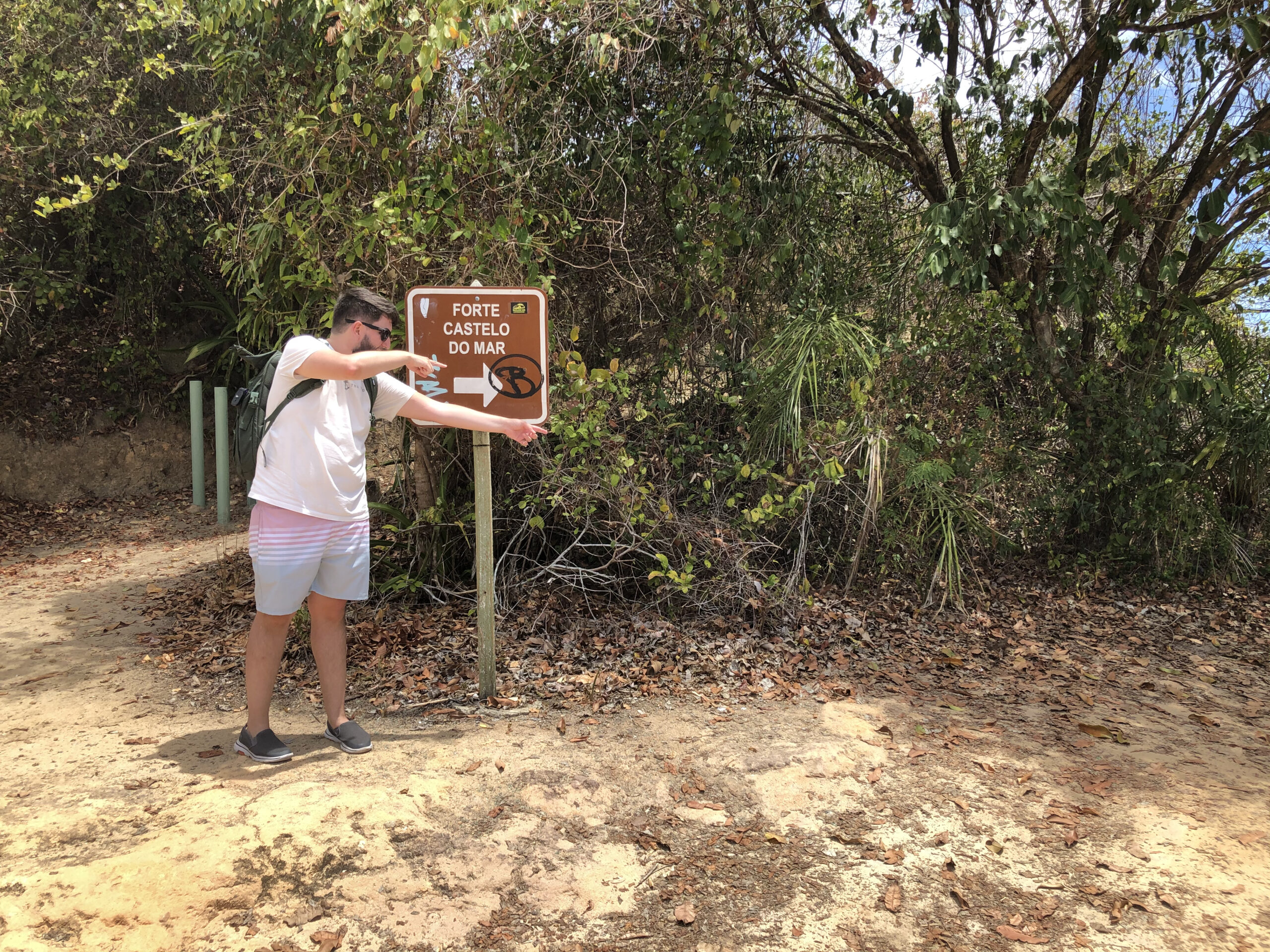 Rudi apontando para a placa de madeira que indica o caminho para o Forte Castelo do Mar