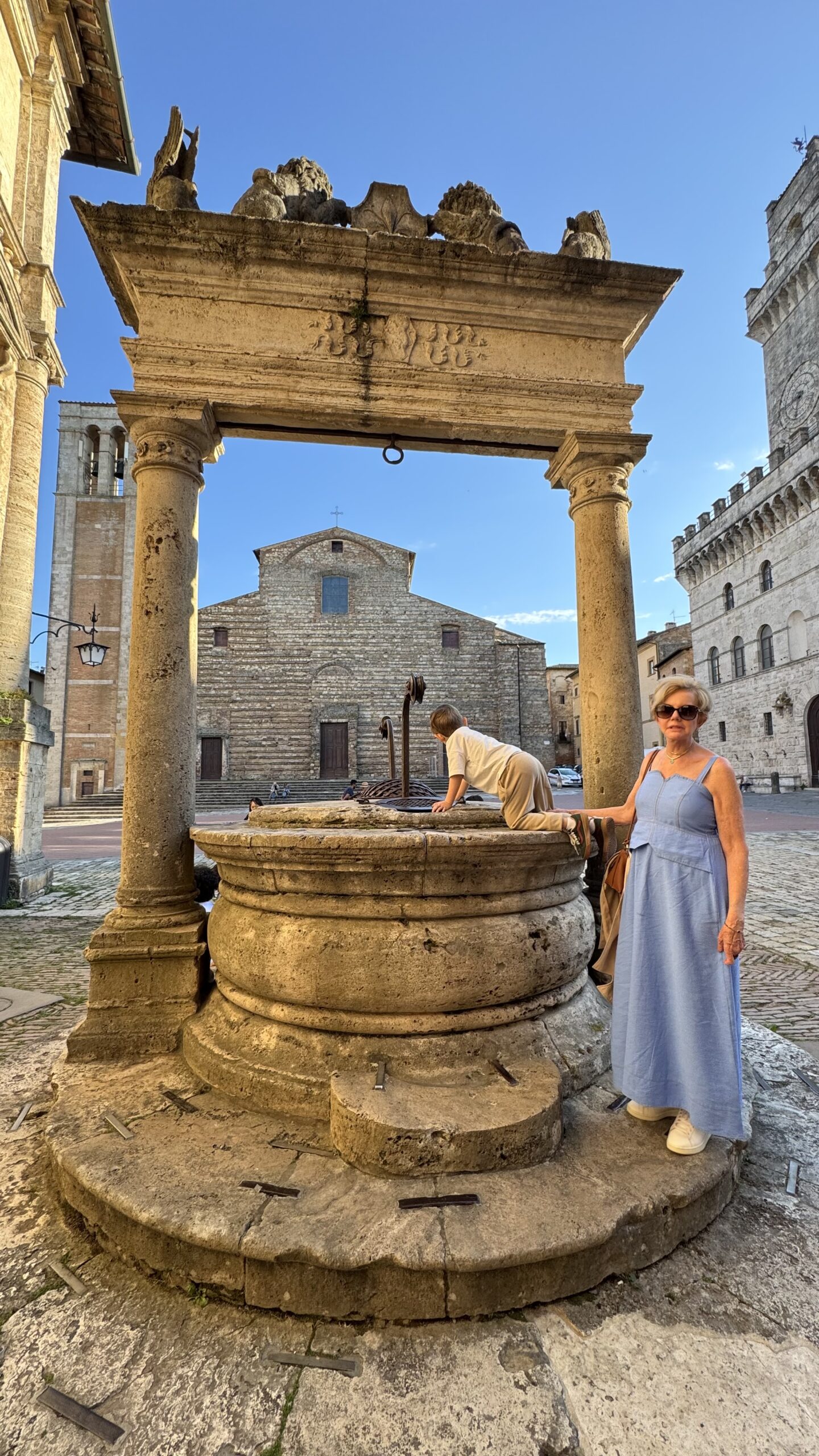 Criança debruçada sobre o poço histórico da Piazza Grande em Montepulciano, com a catedral ao fundo
