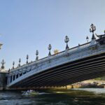 Pont Alexandre III ao entardecer com barco passando pelo Sena