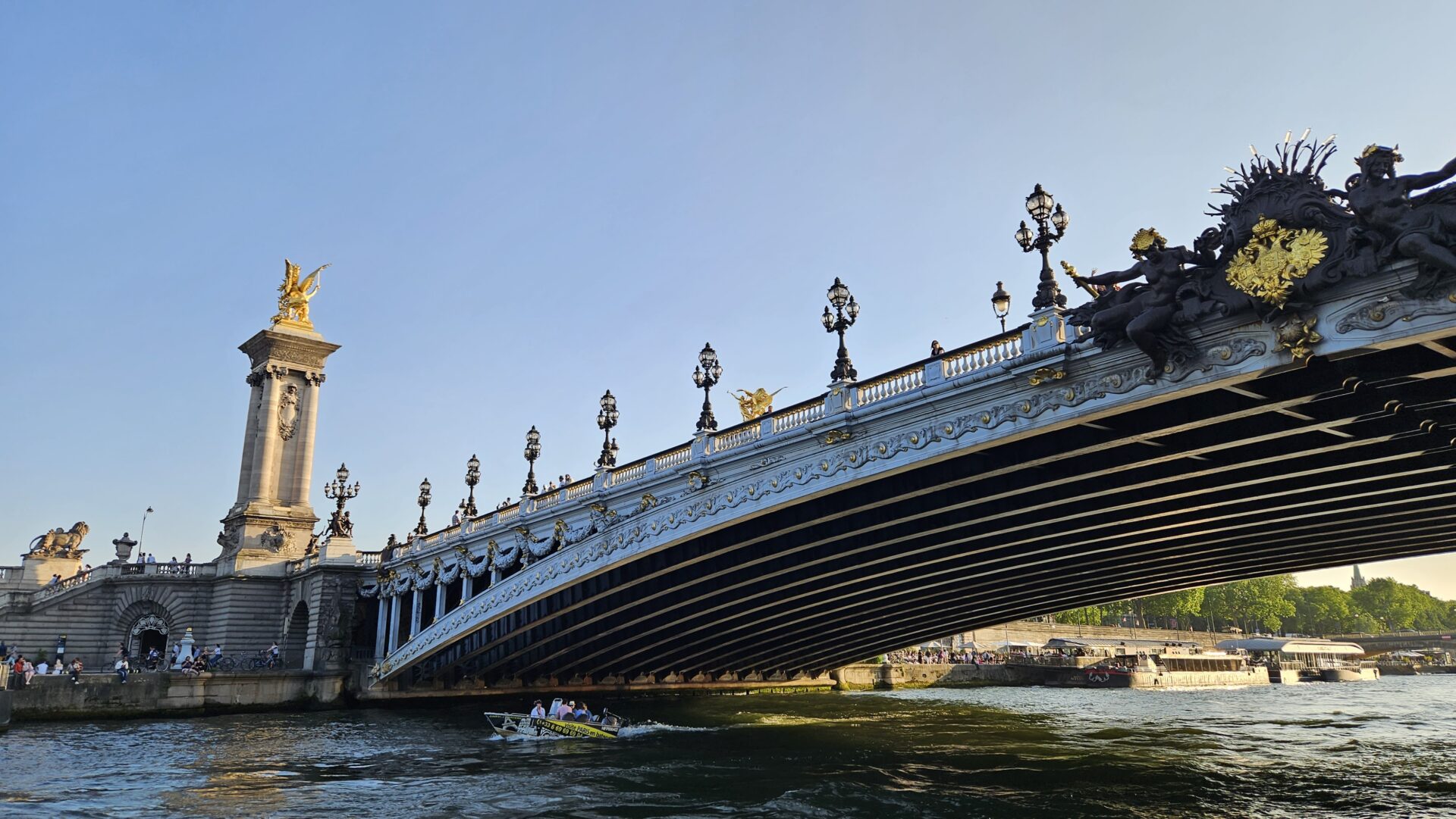 Pont Alexandre III ao entardecer com barco passando pelo Sena