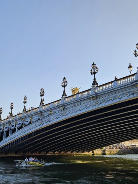 Pont Alexandre III ao entardecer com barco passando pelo Sena