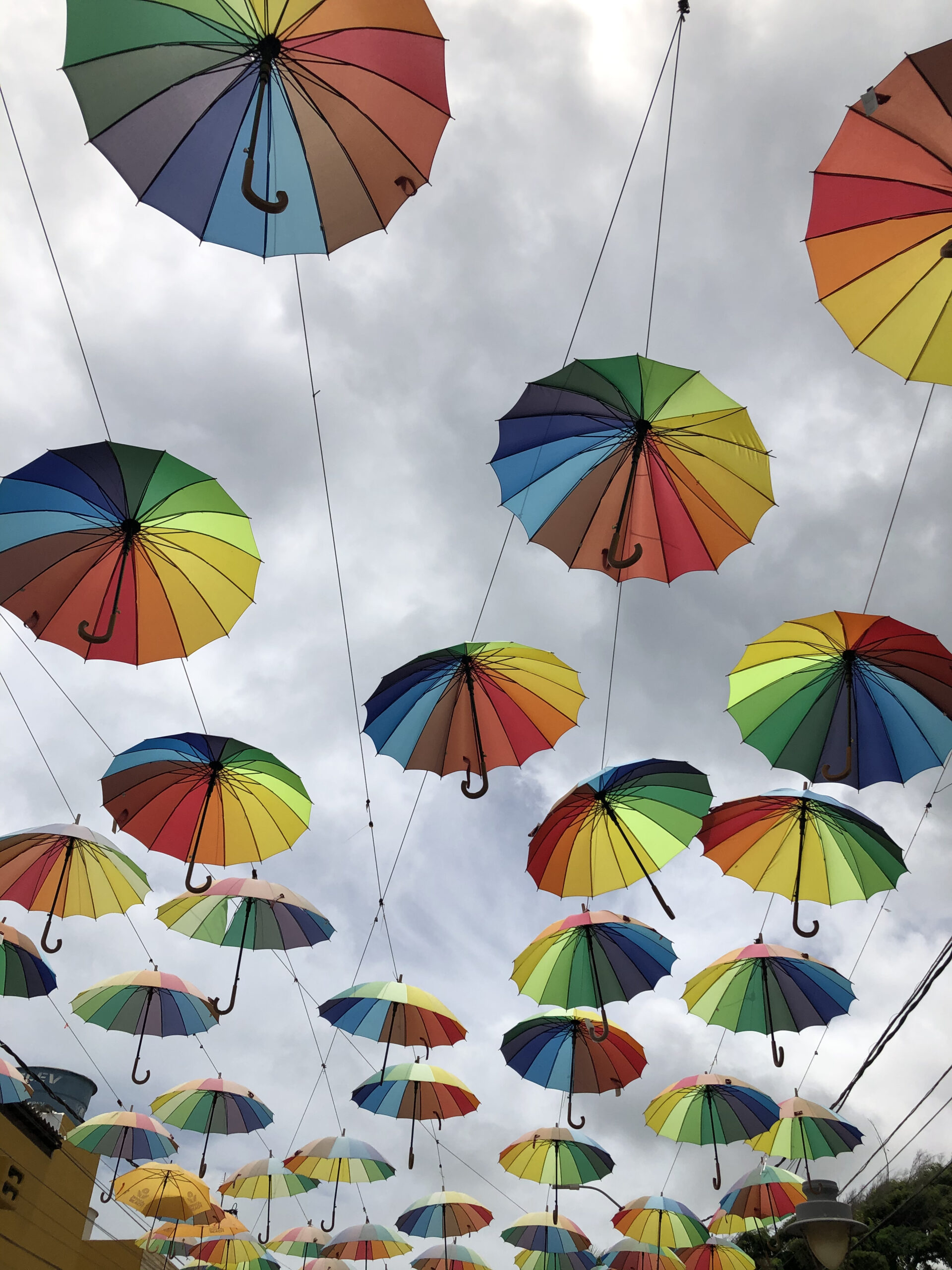 Sombrinhas coloridas penduradas sobre a rua principal da Vila de Porto de Galinhas, com lojas nas laterais