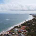 Vista aerea da praia de Porto de Galinhas, com casas de telhado alaranjado na orla e o mar em tons de azul e verde