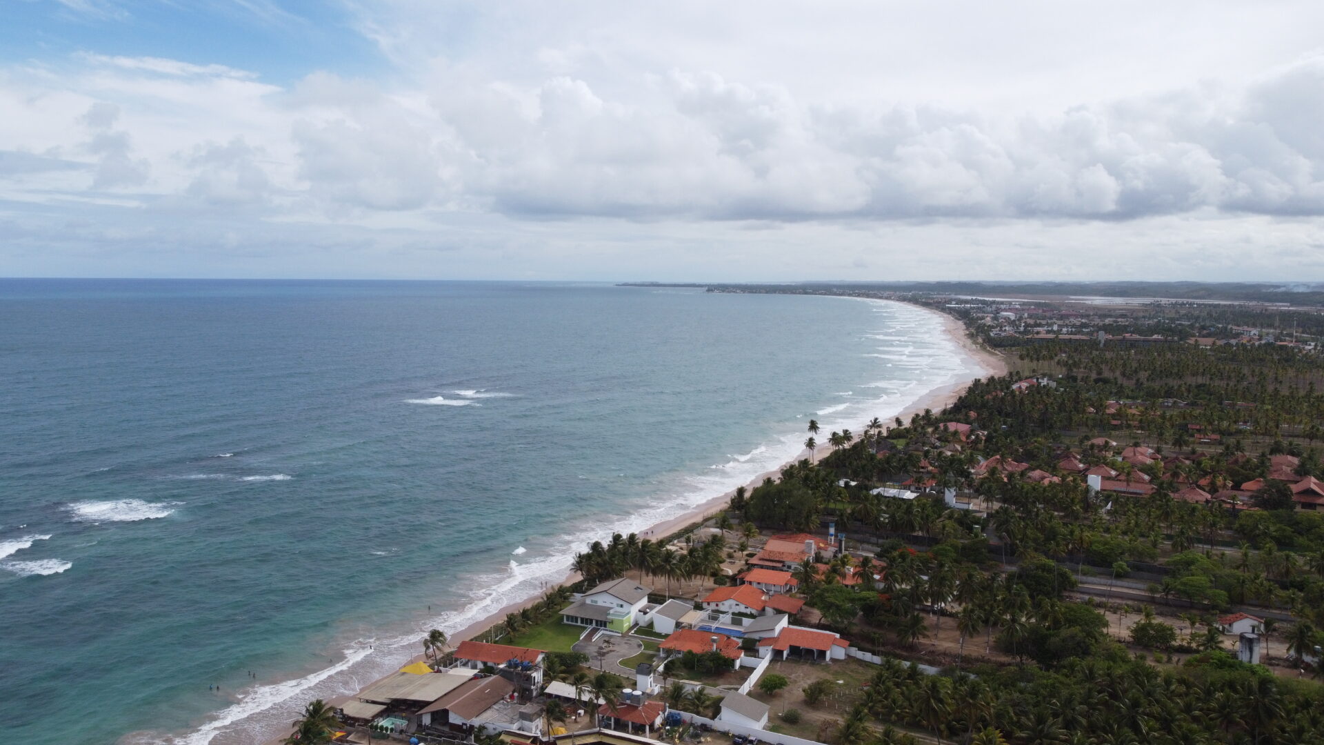 Vista aerea da praia de Porto de Galinhas, com casas de telhado alaranjado na orla e o mar em tons de azul e verde