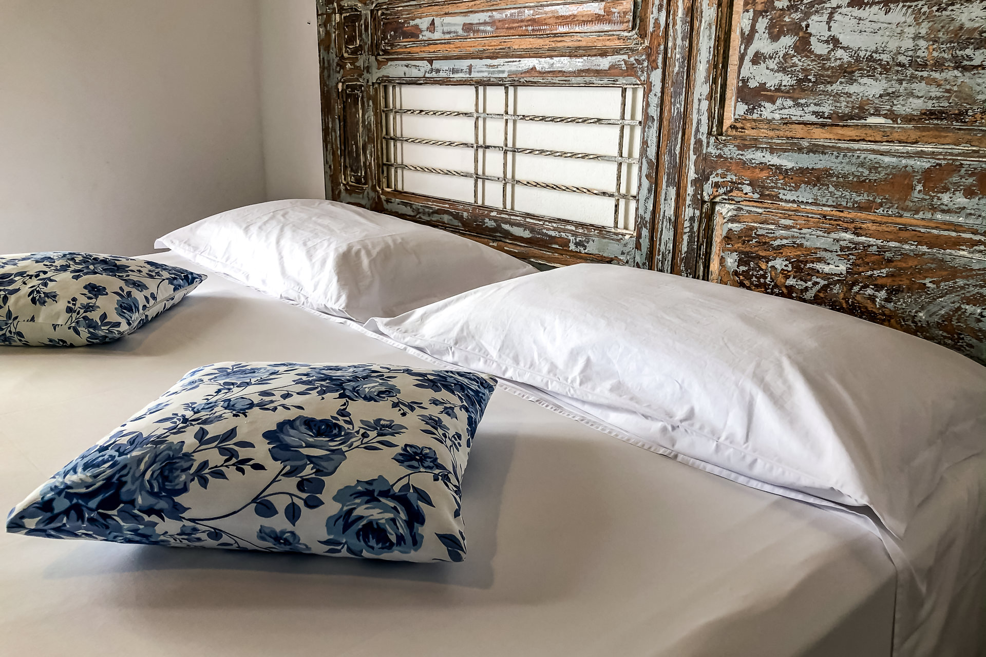 Cama de casal com cabeceira de madeira rústica e almofadas estampadas em azul e branco em um dos chalés da Pousada Casotas