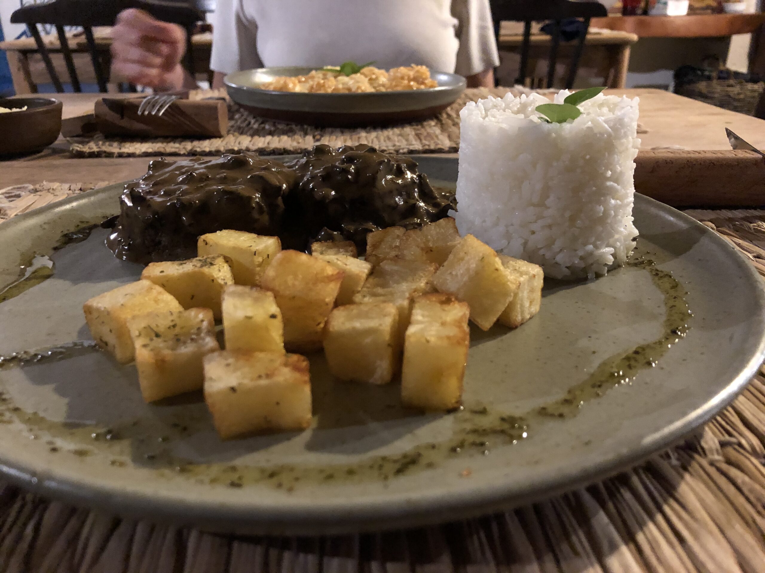 Prato do jantar da Pousada Quadrado de Charme com carne ao molho, mandioca frita e arroz servido em mesa rustica