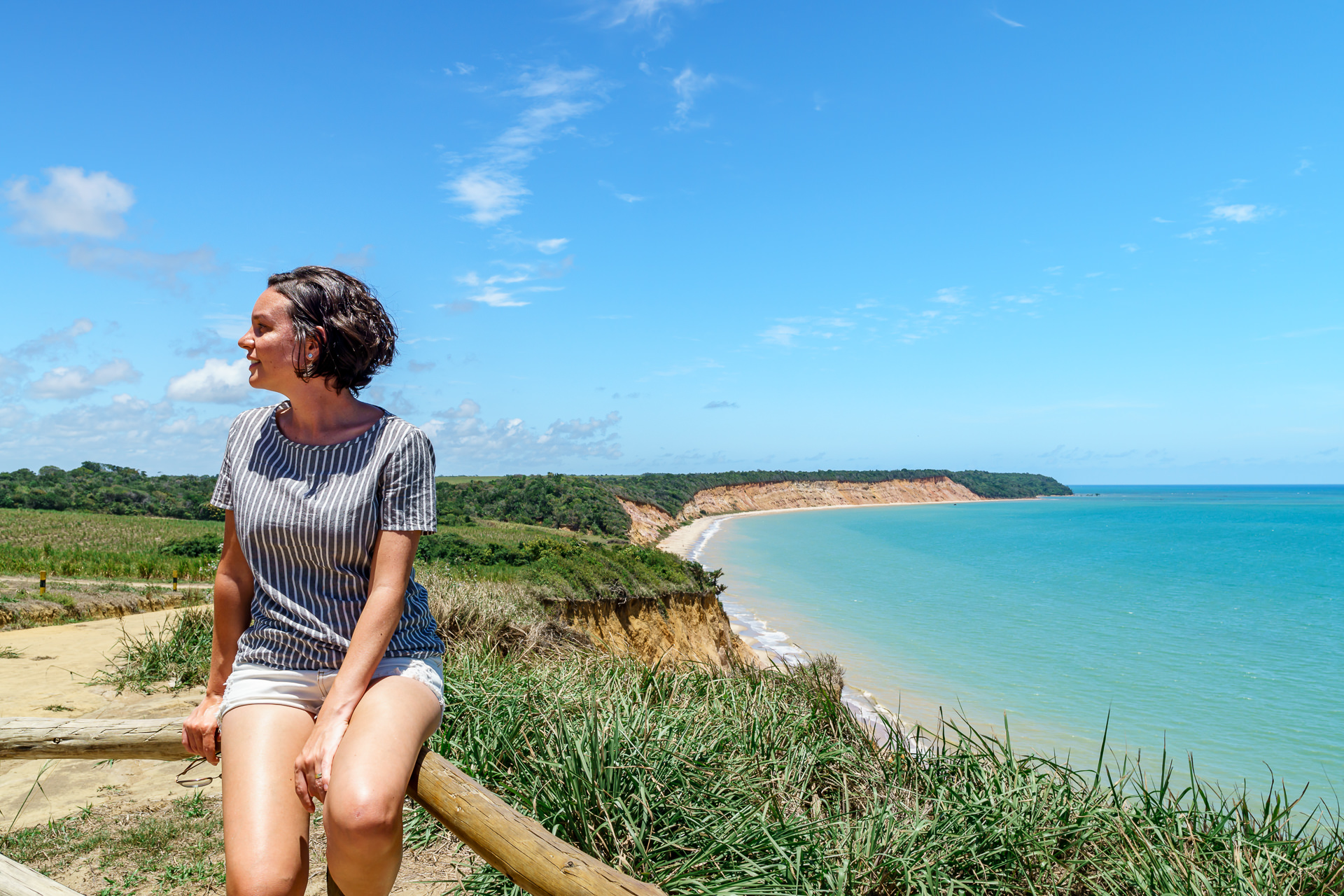Mulher sentada no mirante da Praia do Carro Quebrado, com vista para o mar turquesa e as falésias ao fundo