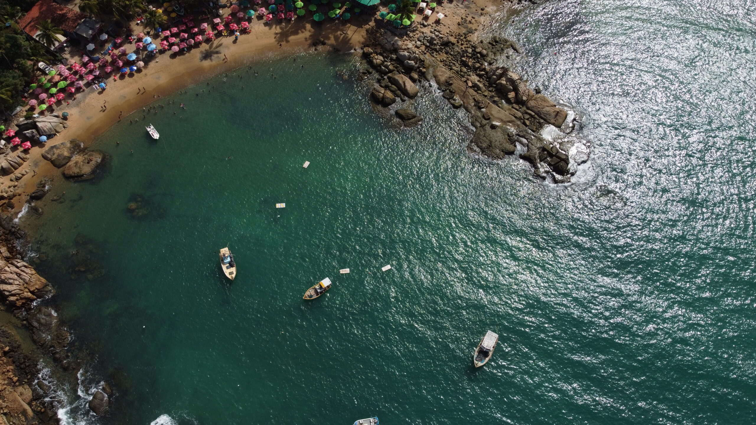 Vista aerea de drone da Praia de Calhetas, enseada de agua turquesa com barracas coloridas na areia