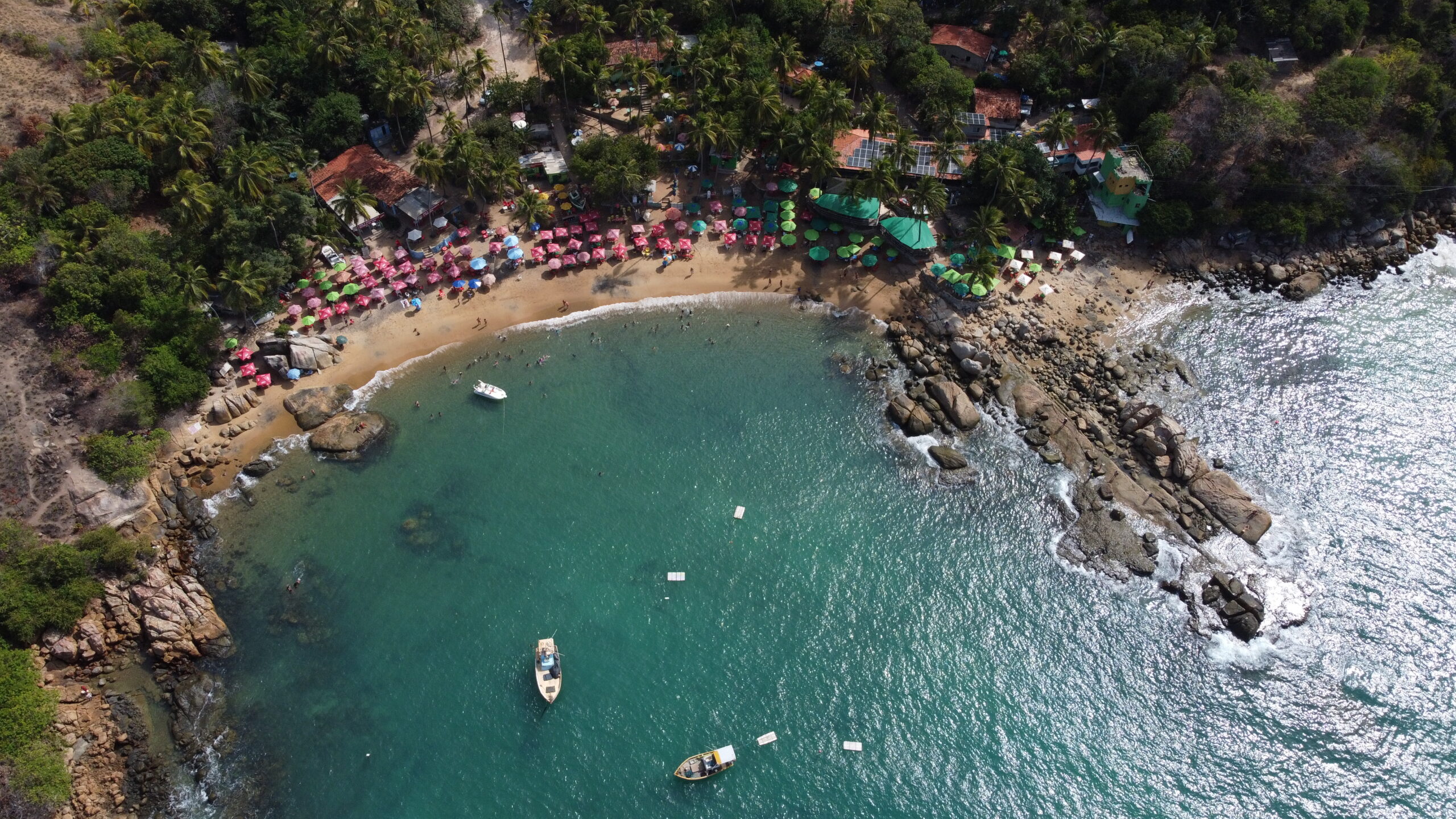 Vista aerea de drone da Praia de Calhetas, enseada com barracas coloridas e mar verde no Cabo de Santo Agostinho