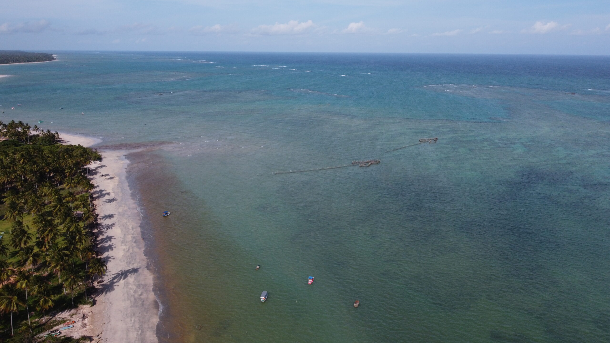 Vista aerea de drone da faixa de recife e das piscinas naturais rasas formadas na mare baixa em frente a Praia do Marceneiro
