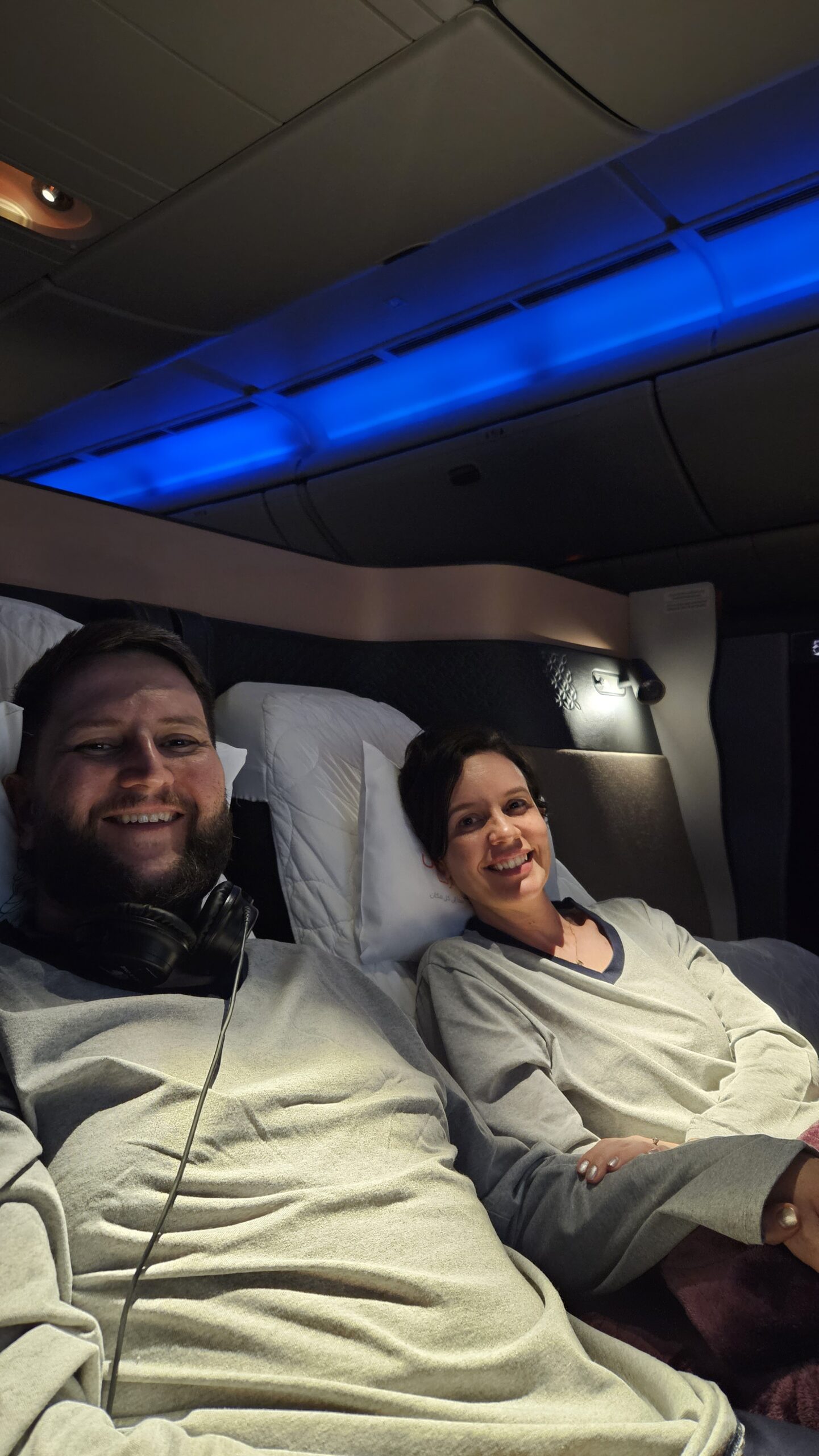Rudi e Carol deitados na cama de casal formada pelos assentos centrais da Qsuite