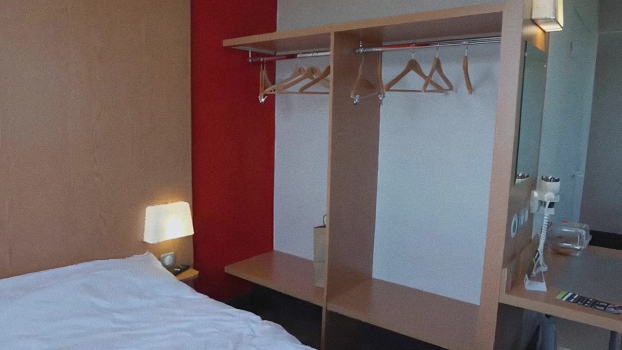 Quarto do B&B Hotel Disneyland Paris com cama, parede vermelha e guarda-roupa aberto com cabides