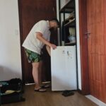 Homem mexendo no frigobar do quarto na Pousada Luar da Ilha, com armário amplo ao fundo