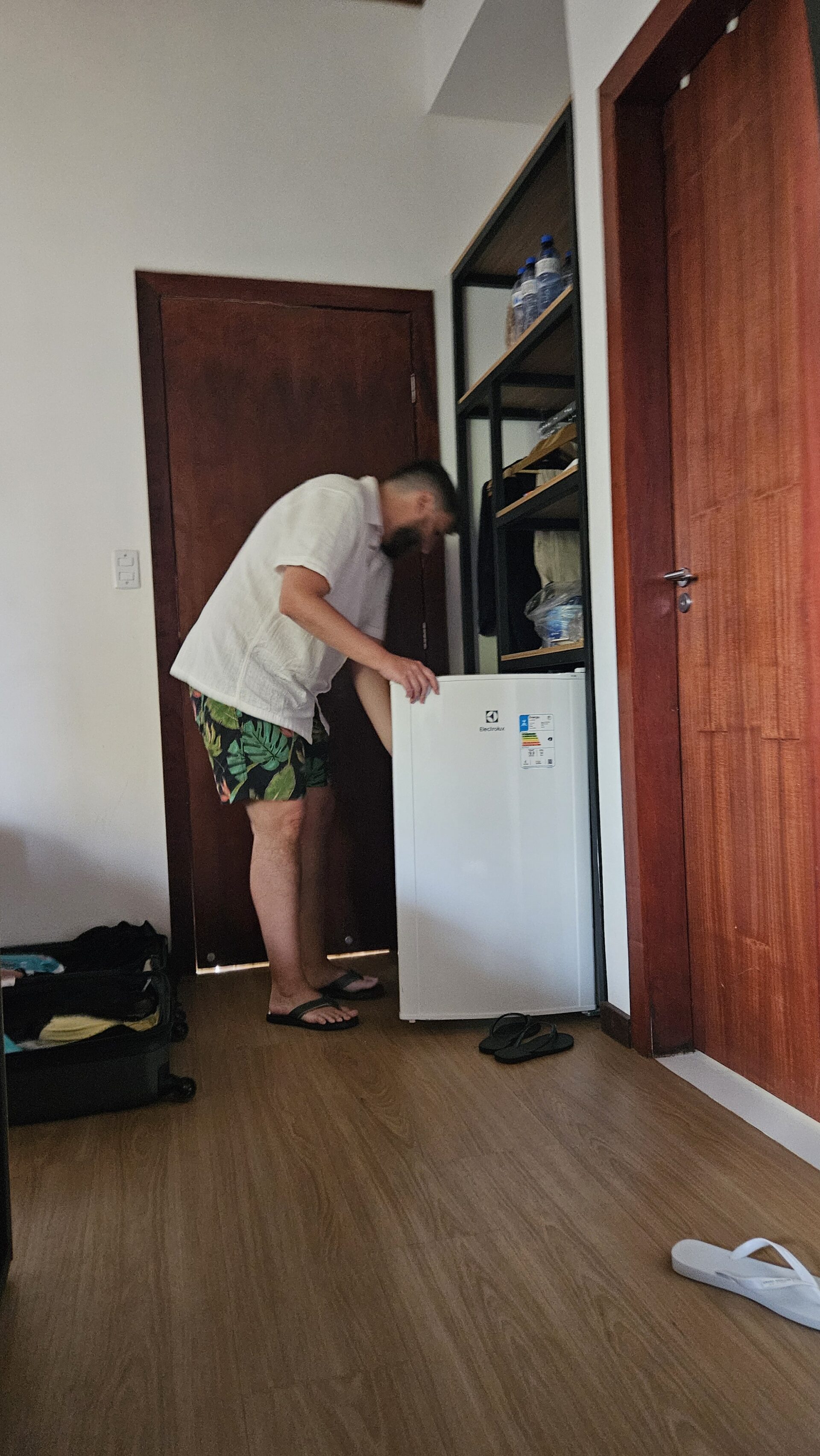 Homem mexendo no frigobar do quarto na Pousada Luar da Ilha, com armário amplo ao fundo