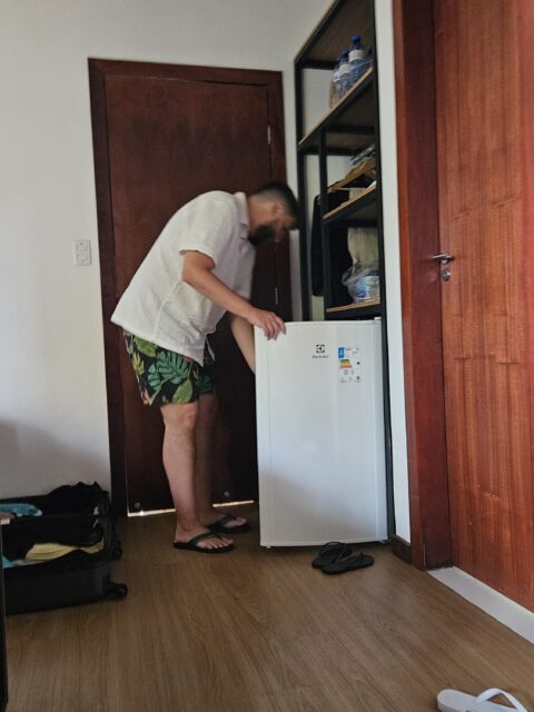 Homem mexendo no frigobar do quarto na Pousada Luar da Ilha, com armário amplo ao fundo