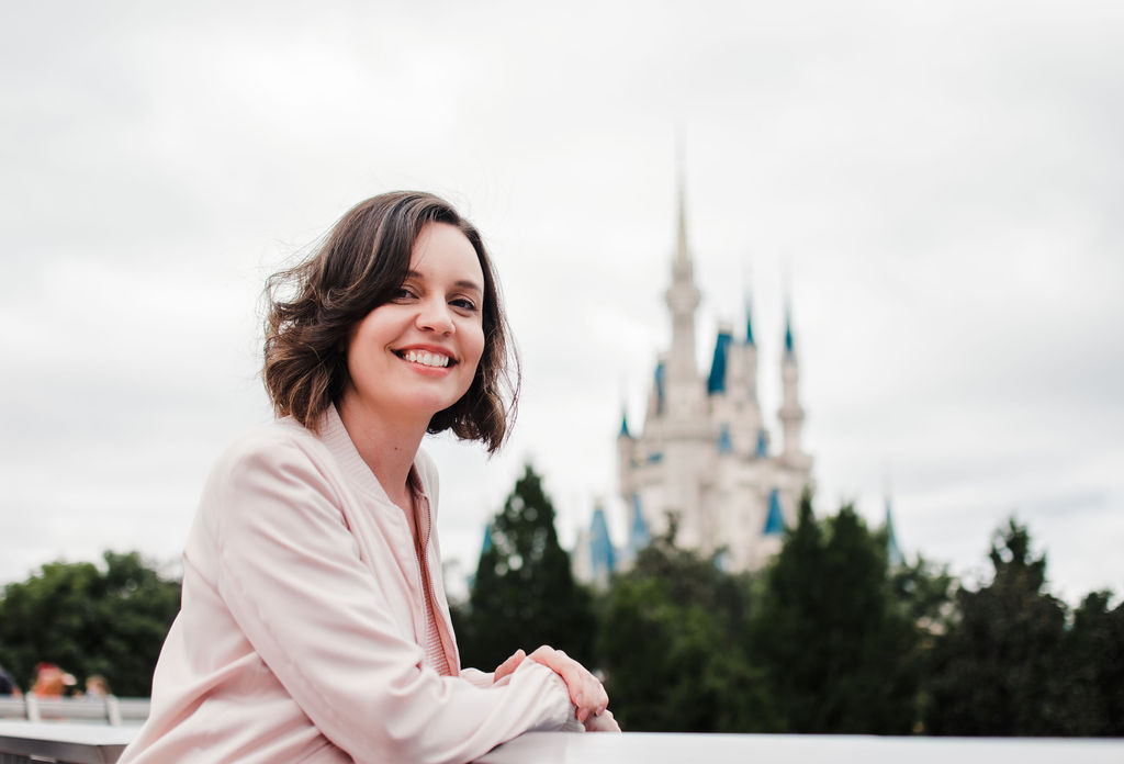 Retrato da Carol sorrindo apoiada na grade com o Castelo da Cinderela ao fundo