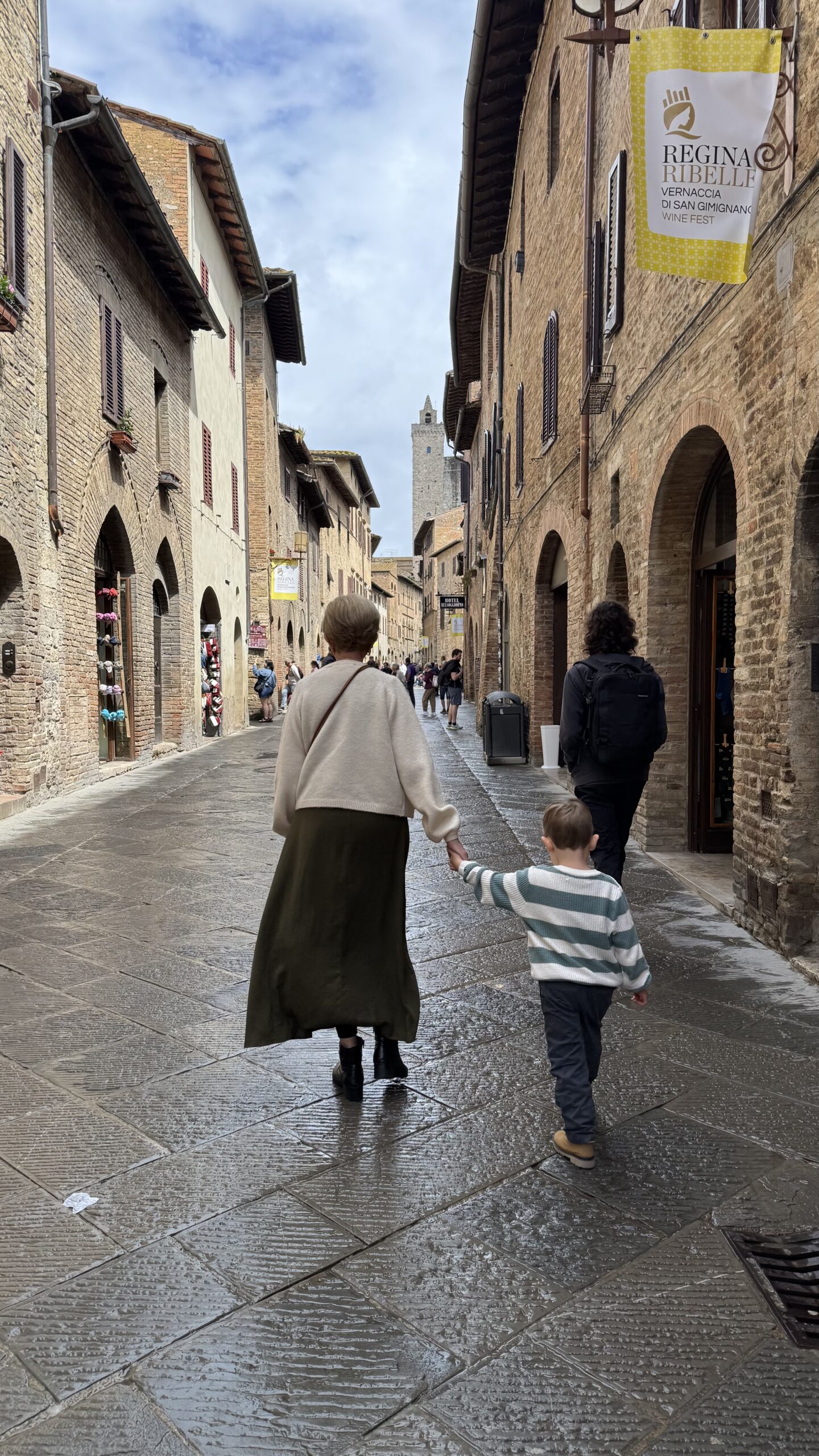 Família caminhando por uma rua medieval de San Gimignano, com as torres da cidade visíveis ao fundo