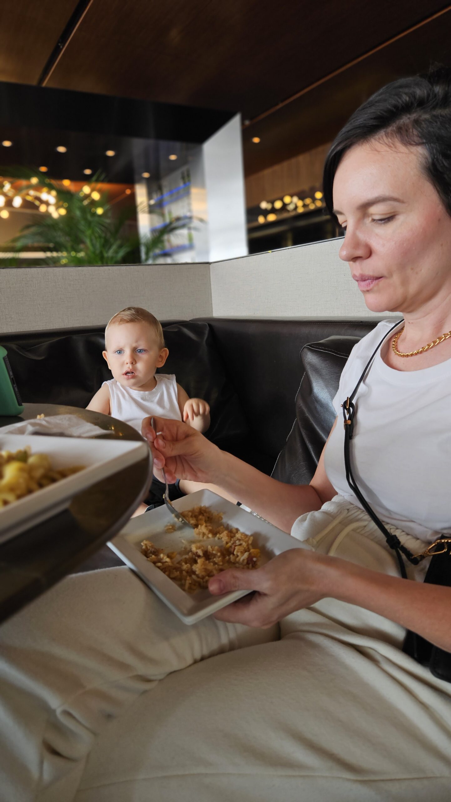 Carol dando comida do buffet para Samuel na Sala VIP Club de Brasília, com pratos do café da manhã