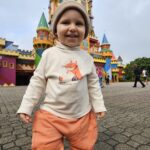 Sam sozinho e sorridente em frente ao castelo na entrada do parque
