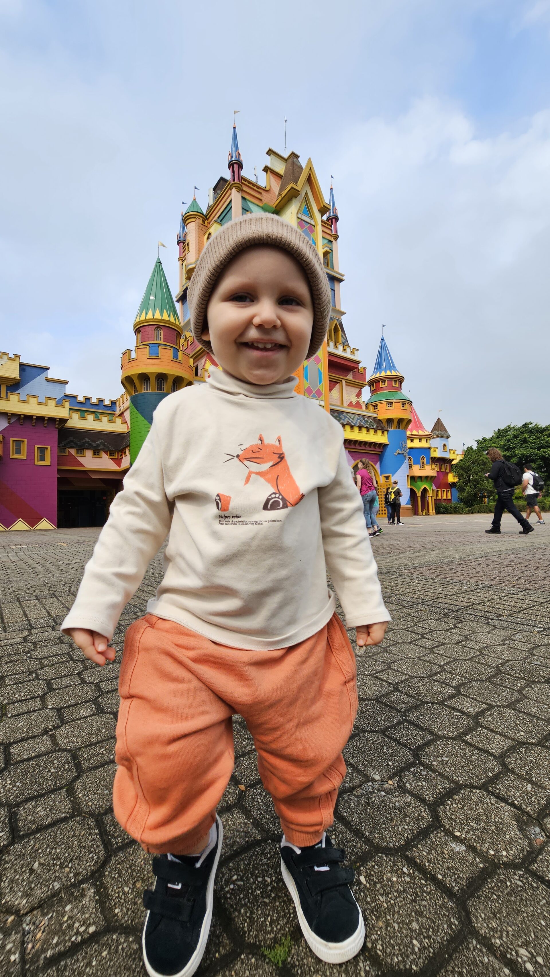 Sam sozinho e sorridente em frente ao castelo na entrada do parque