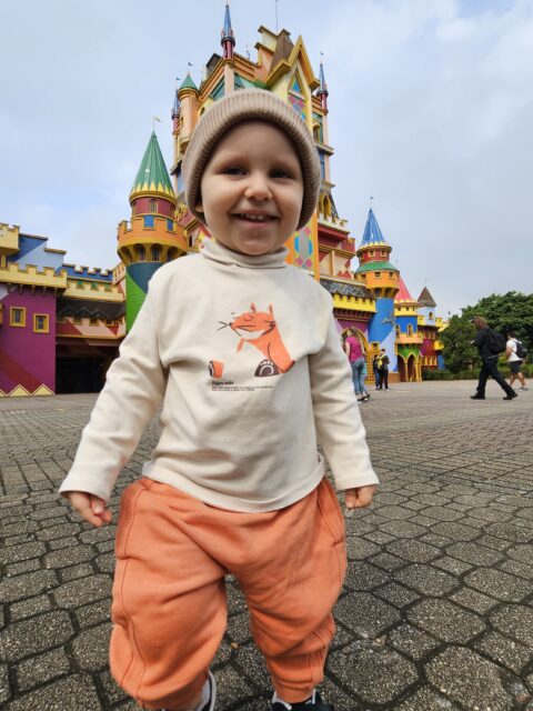 Sam sozinho e sorridente em frente ao castelo na entrada do parque