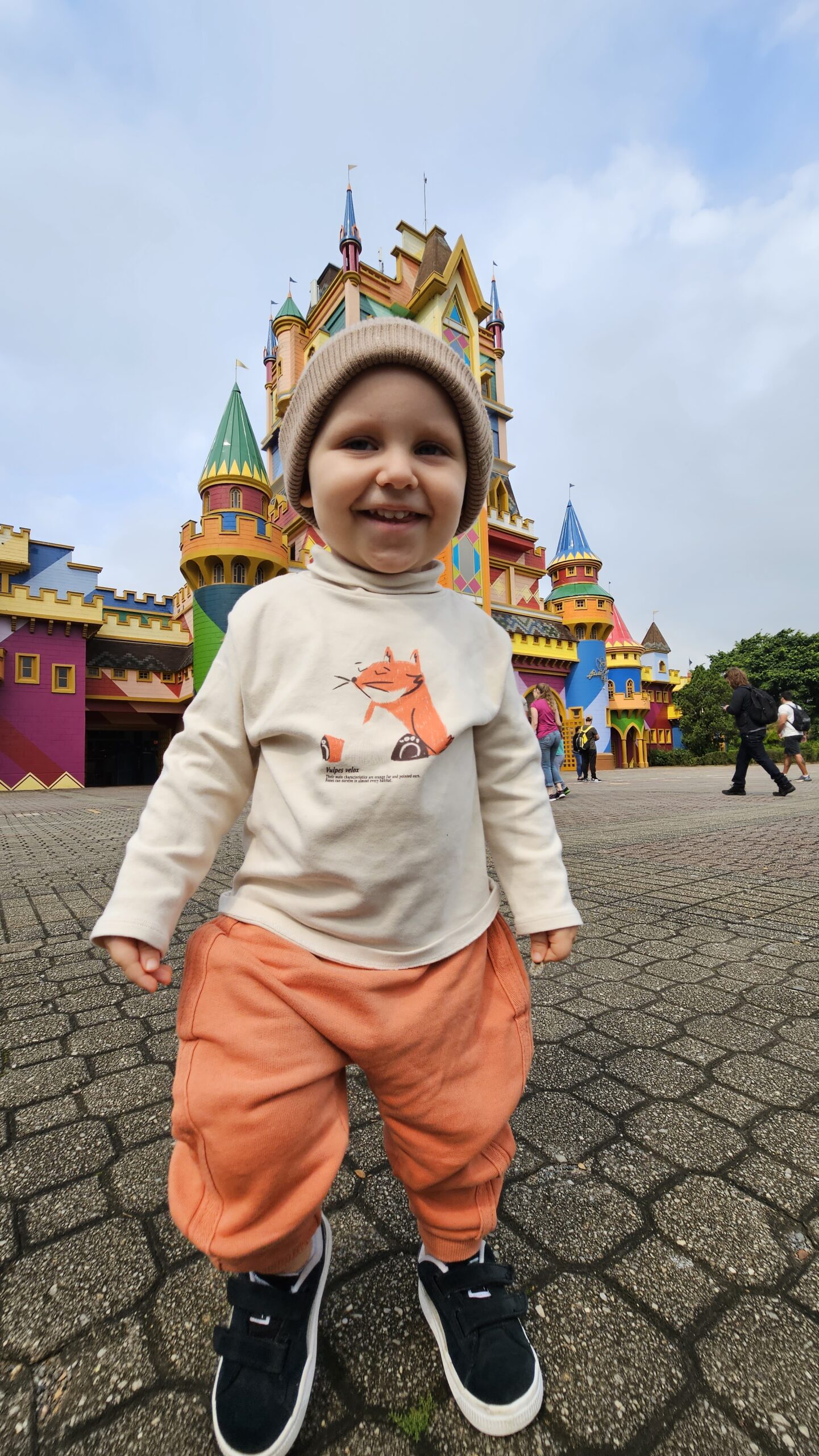 Sam sozinho e sorridente em frente ao castelo na entrada do parque