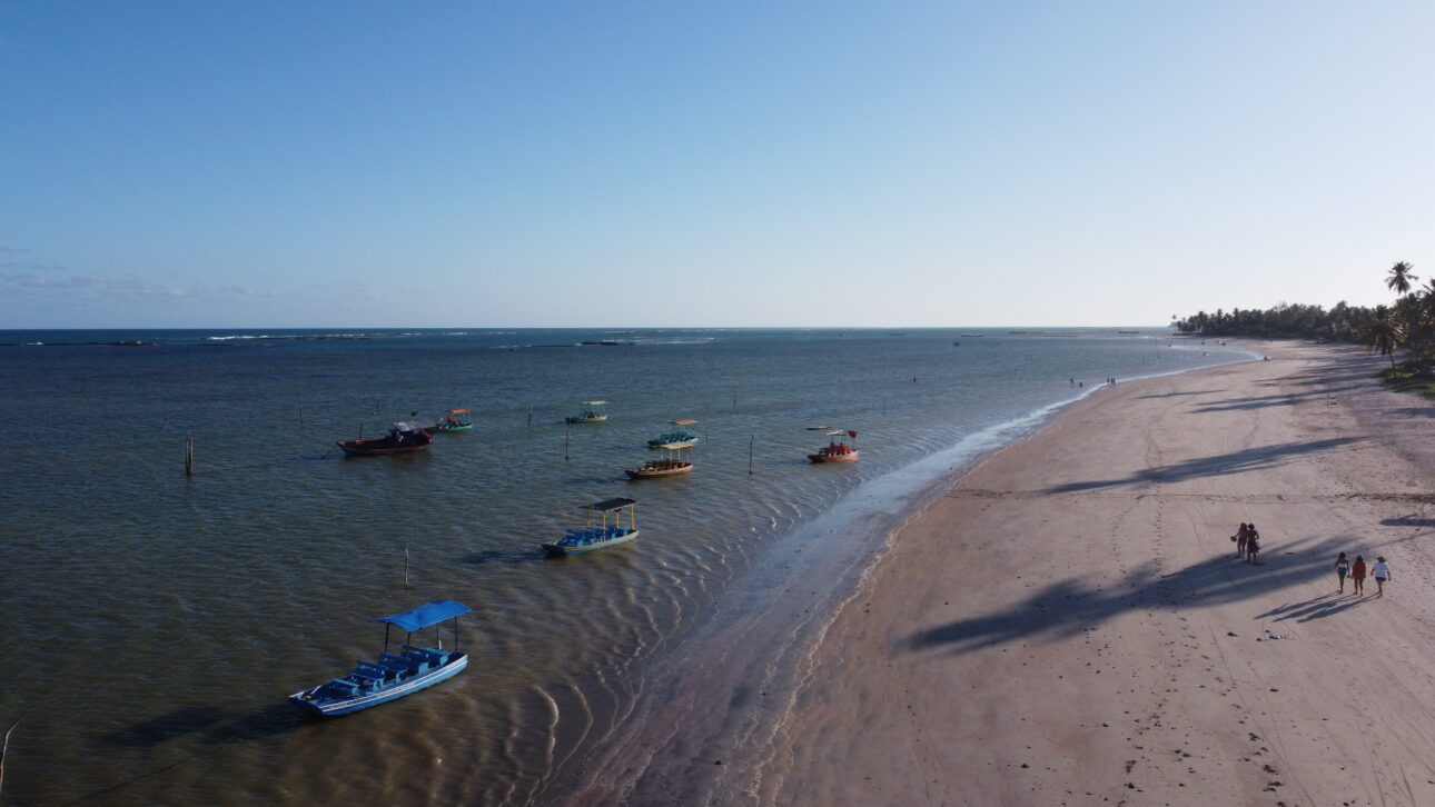 Vista aérea da praia de São Miguel dos Milagres ao entardecer com jangadas na maré baixa