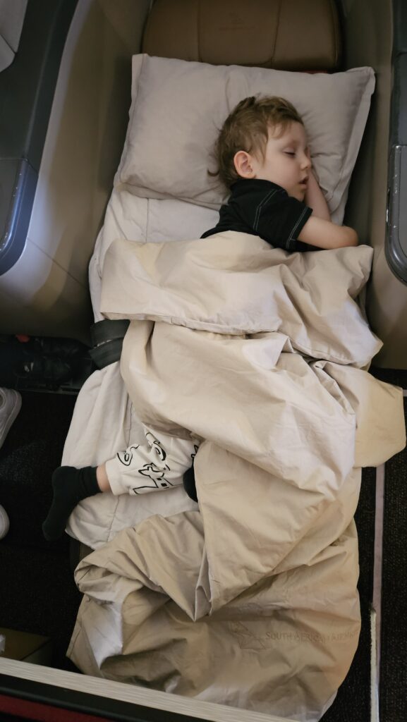Sam dormindo coberto na poltrona-cama da Classe Executiva da South African Airways