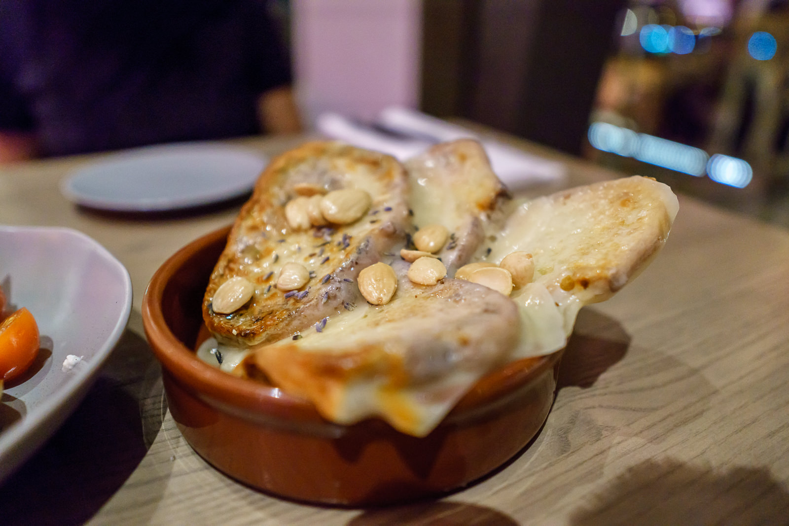 Tábua de pão torrado com queijo derretido e amêndoas, servida em uma travessa de barro no restaurante Toledo