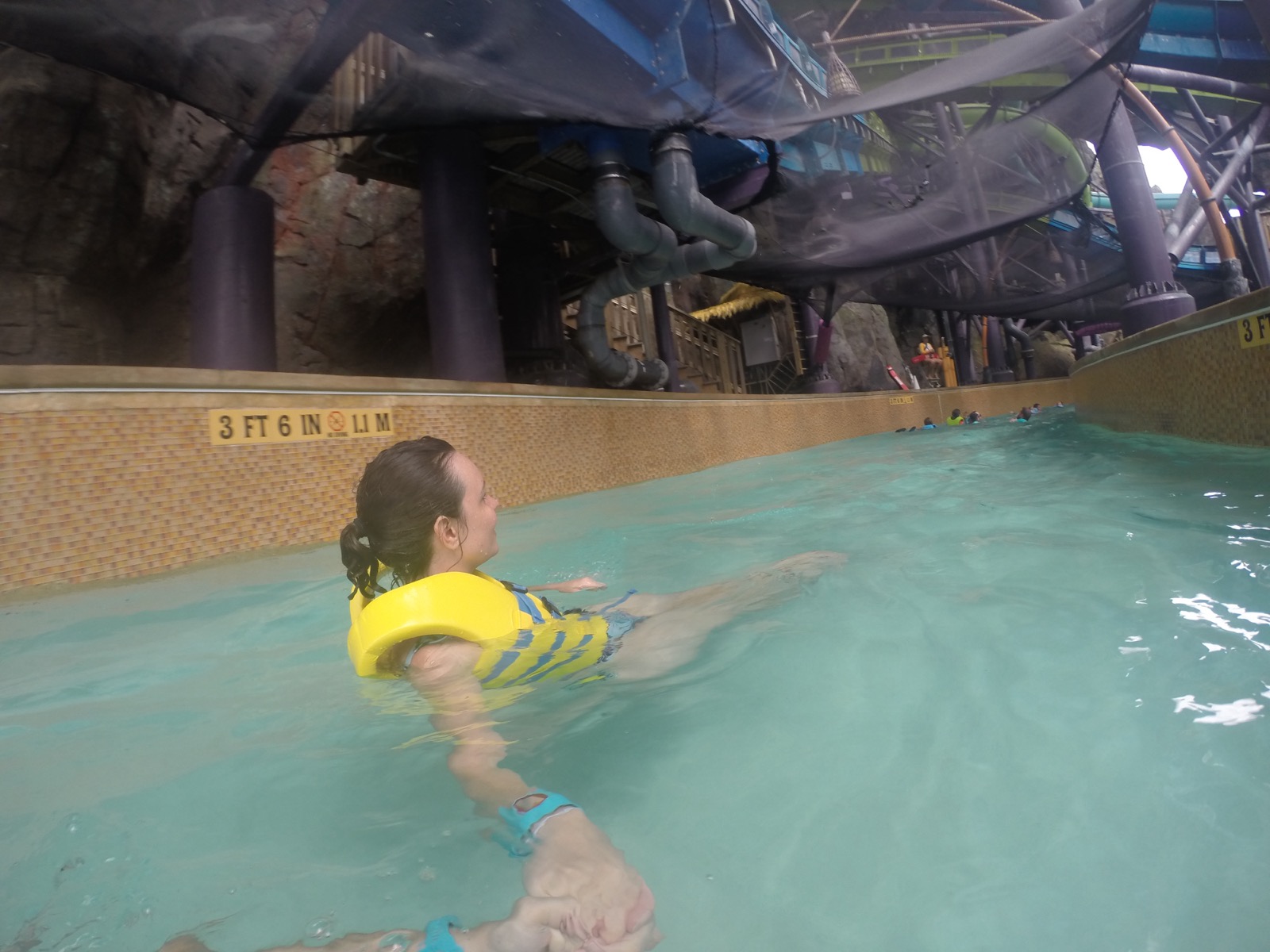 Mulher de colete salva-vidas boiando em piscina do Volcano Bay sob estrutura de toboaguas