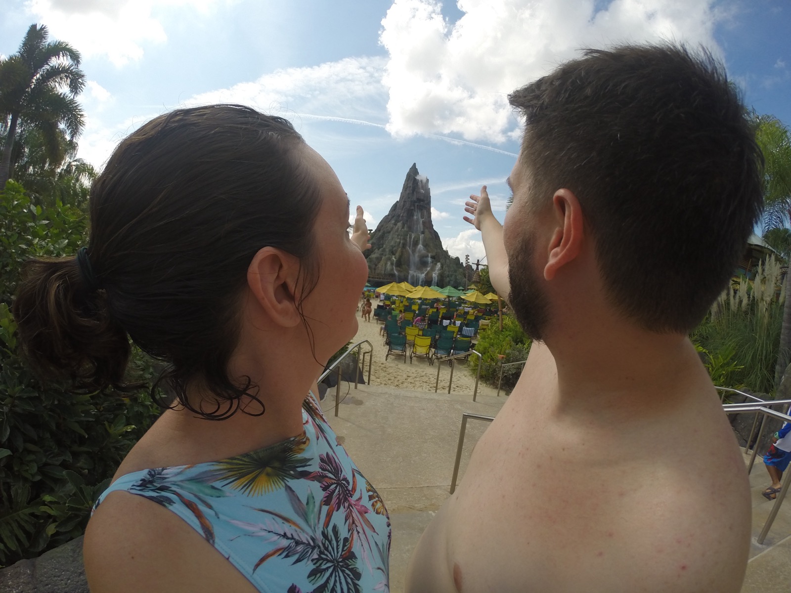 Casal apontando para o vulcao Krakatau no Volcano Bay com espreguicadeiras e guarda-sois ao fundo