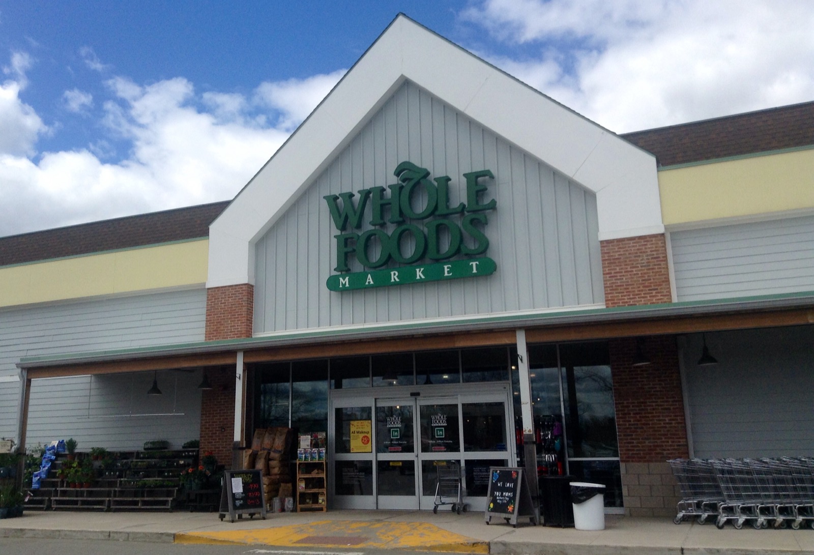 Fachada de uma loja Whole Foods Market com letreiro verde e carrinhos na entrada