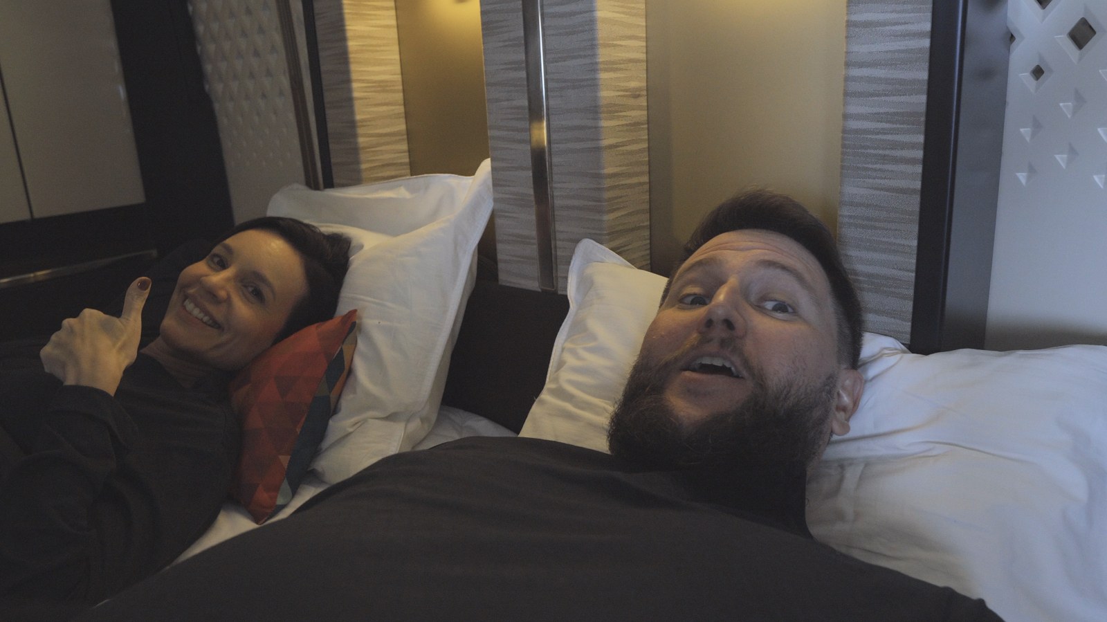 Rudi e Carol deitados na cama da Primeira Classe da Etihad