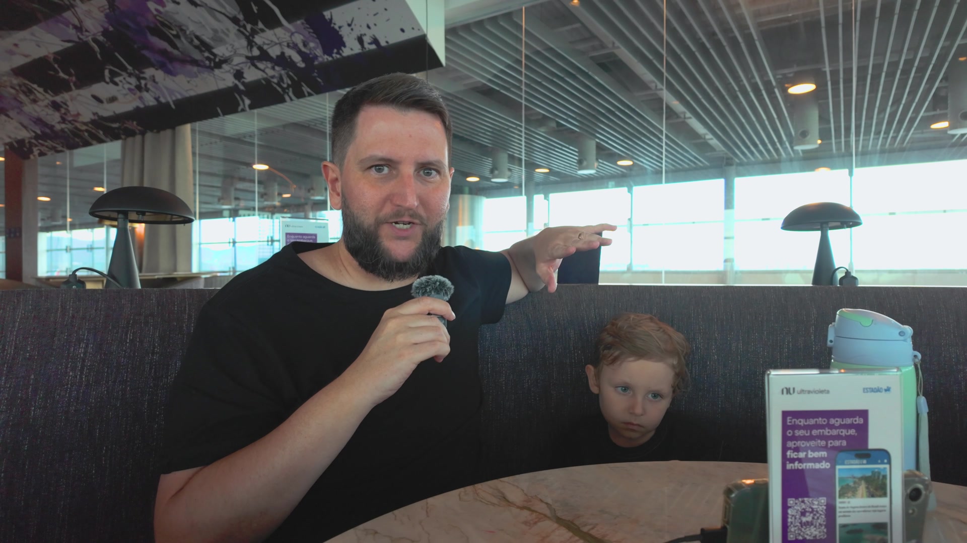 Rudi e o Sam sentados à mesa no Nubank Ultravioleta Lounge, em Guarulhos